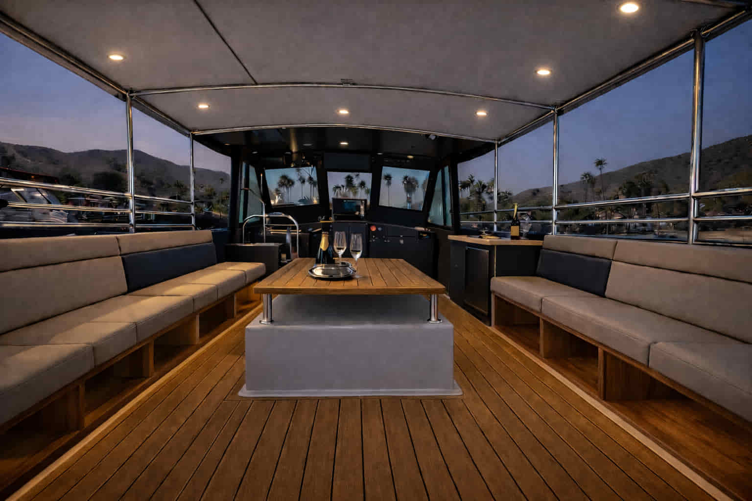 Teak table and wraparound seating inside Aurora Sol, a private harbor cruise boat in Marina del Rey at dusk
